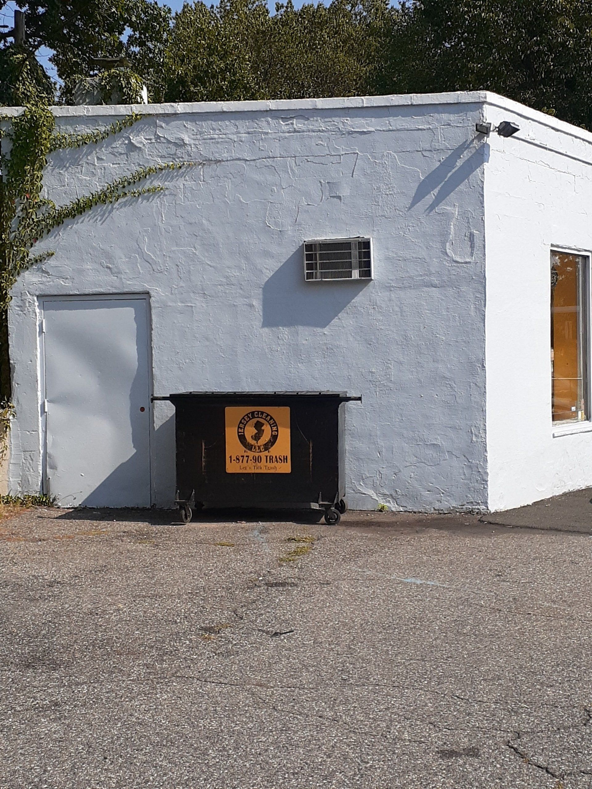 A white building with a black dumpster in front of it