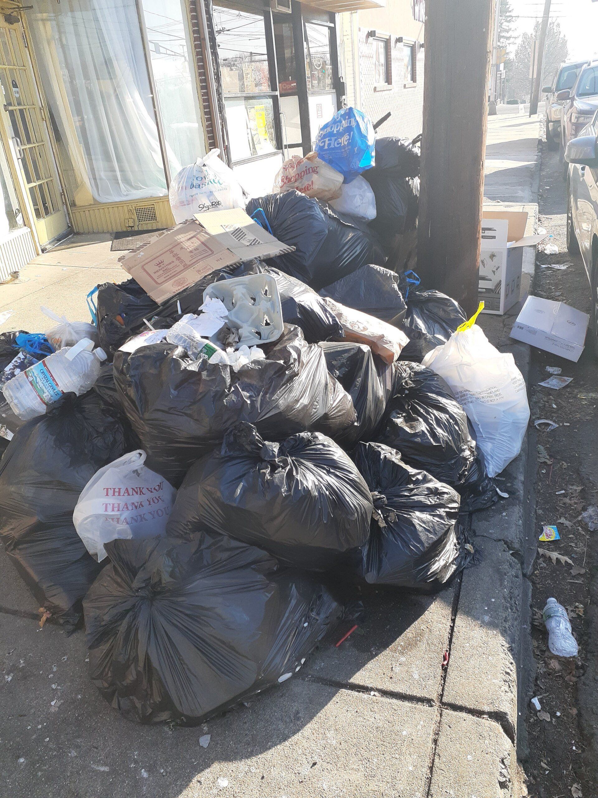 A pile of trash is sitting on the sidewalk next to a pole.