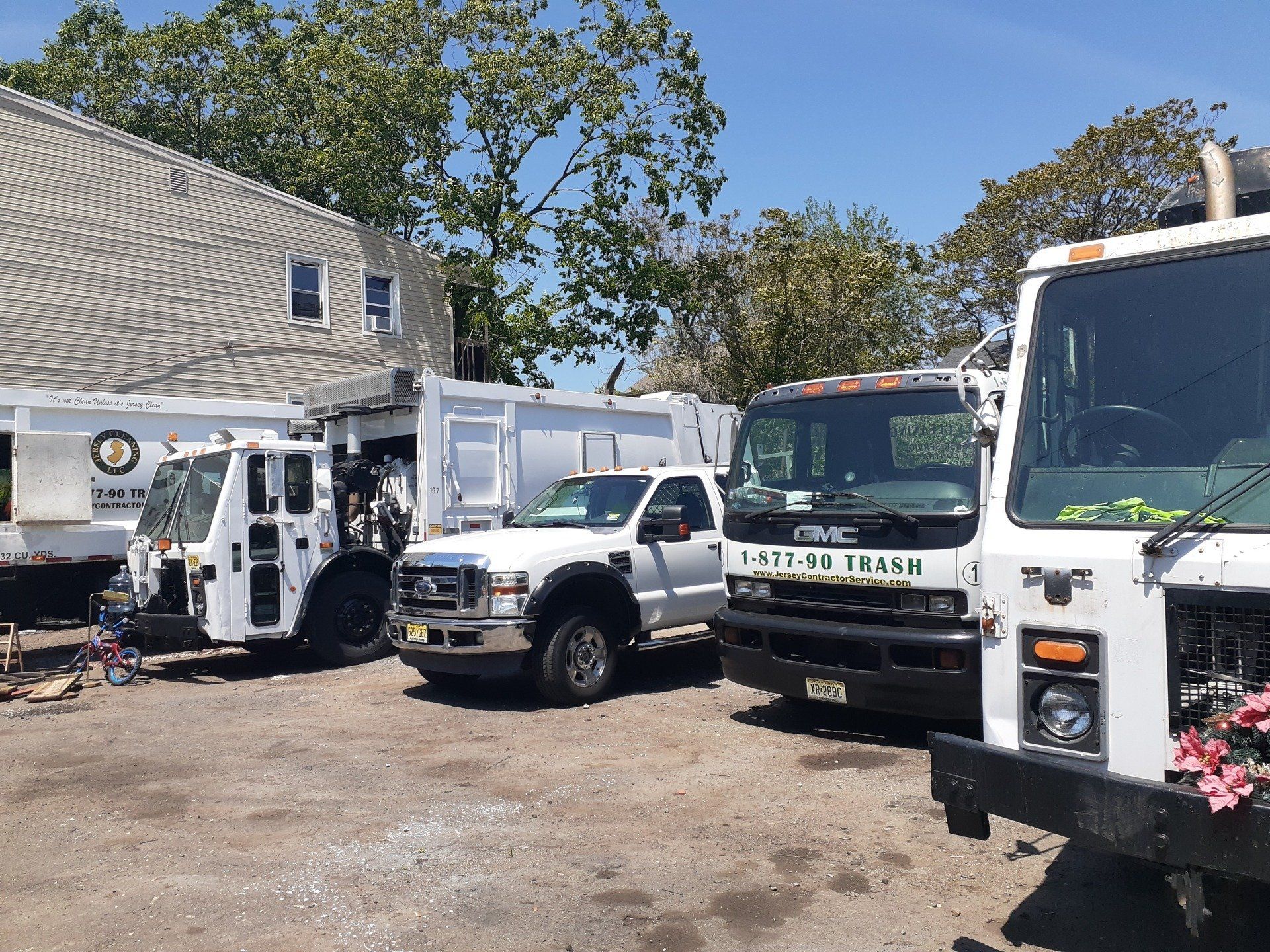 A row of Jersey Cleaning garbage trucks are parked in a parking lot.
