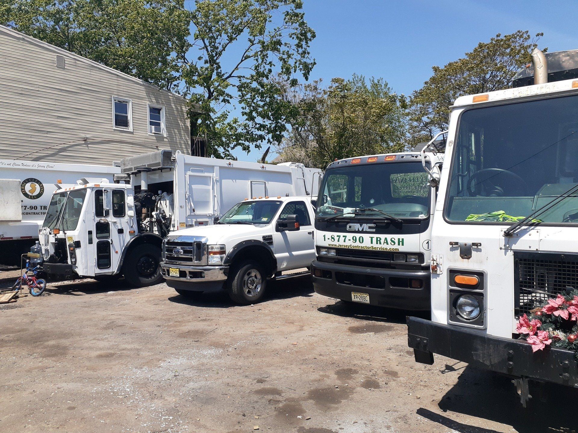 A row of garbage trucks at Jersey Cleaning are parked in a parking lot