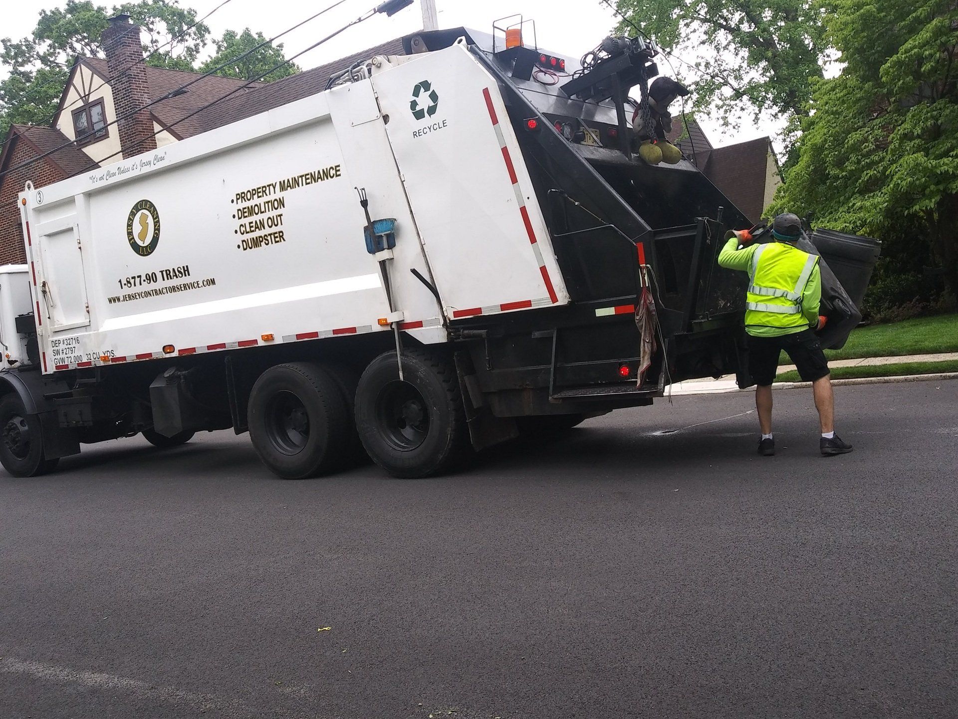 A man in a yellow vest is pushing a garbage truck.