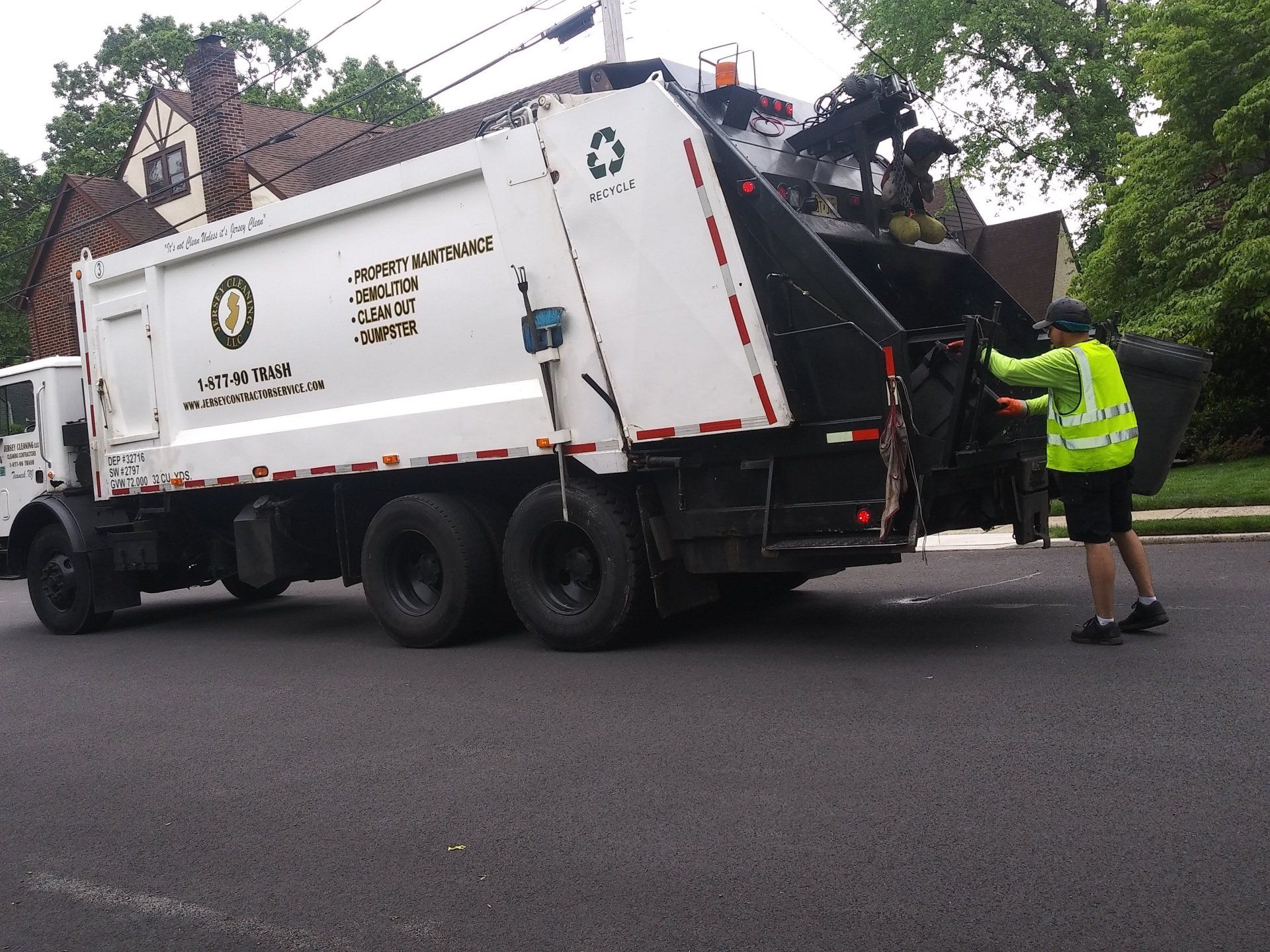 A man in a yellow vest pushes a garbage truck