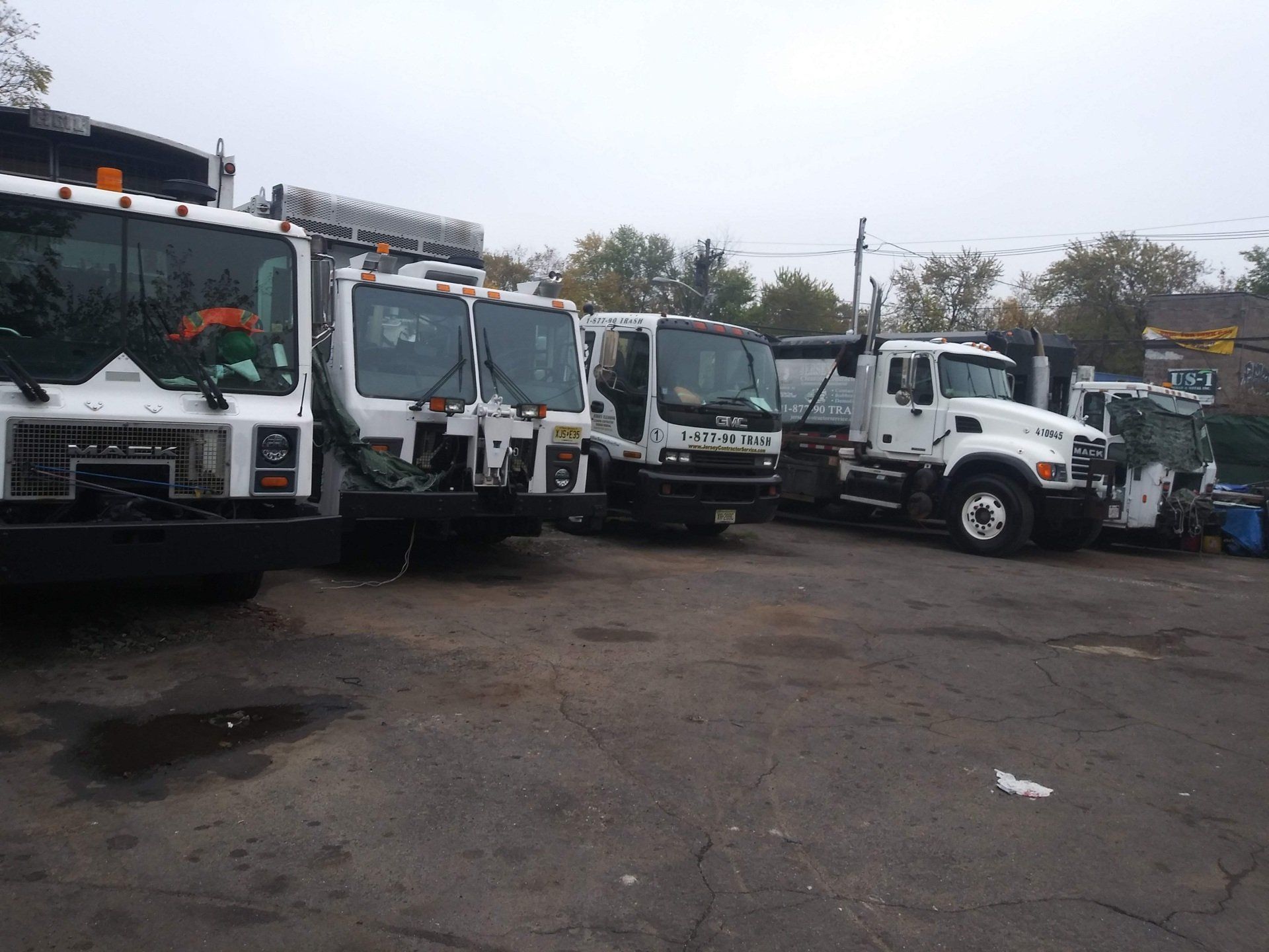 A row of garbage trucks are parked in a parking lot