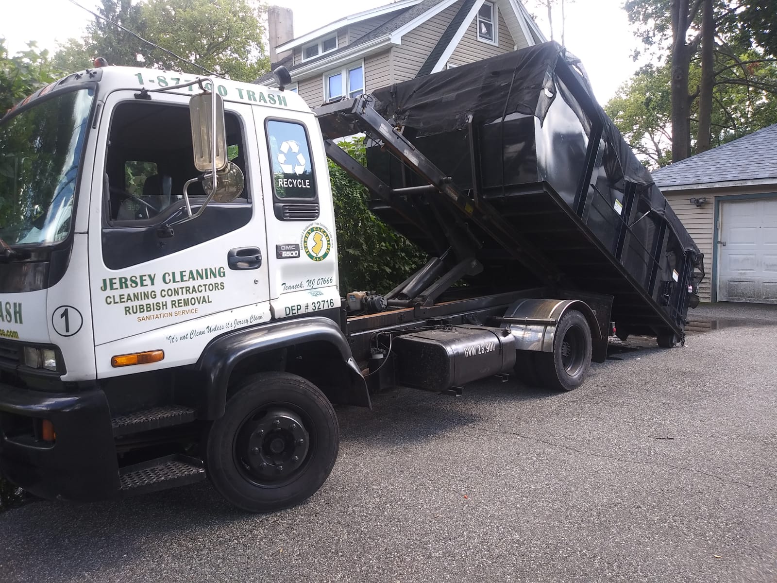 A Jersey Cleaning dumpster truck is parked in front of a house.