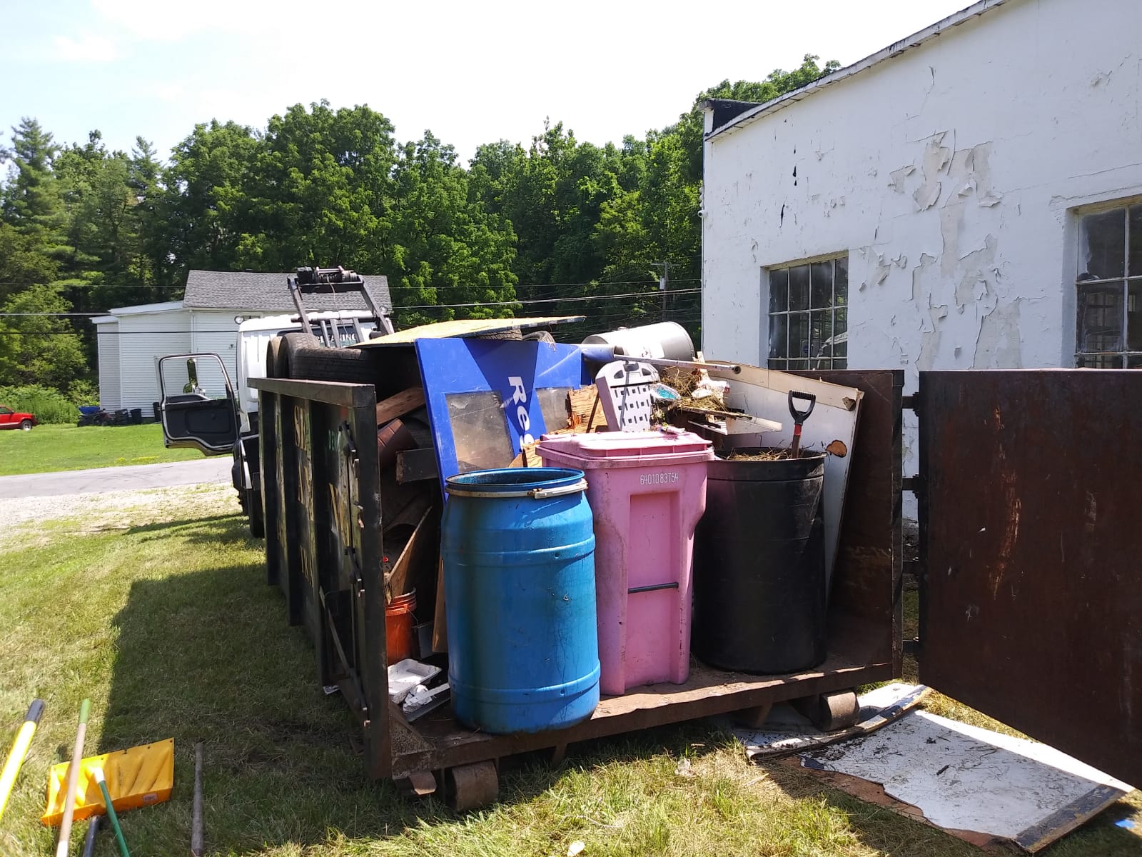 A dumpster filled with a bunch of trash including a pink trash can.