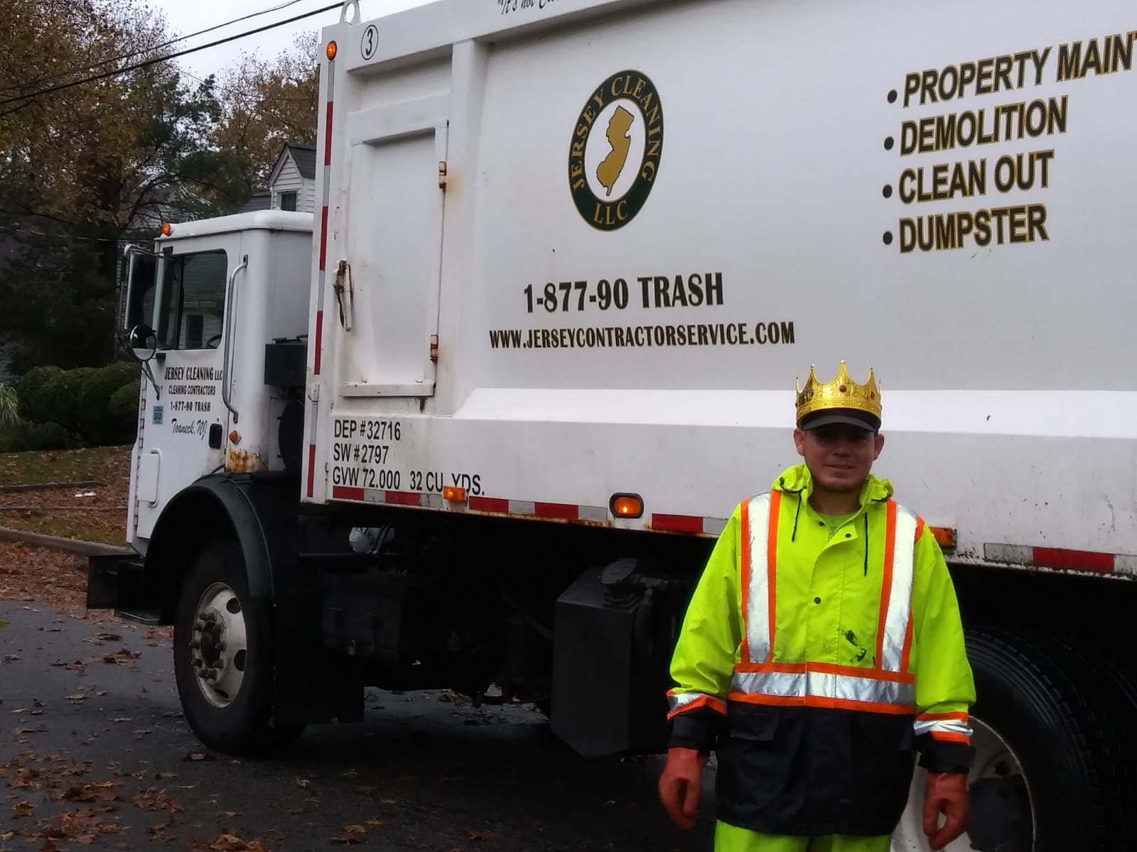 A man wearing a crown stands in front of a trash truck