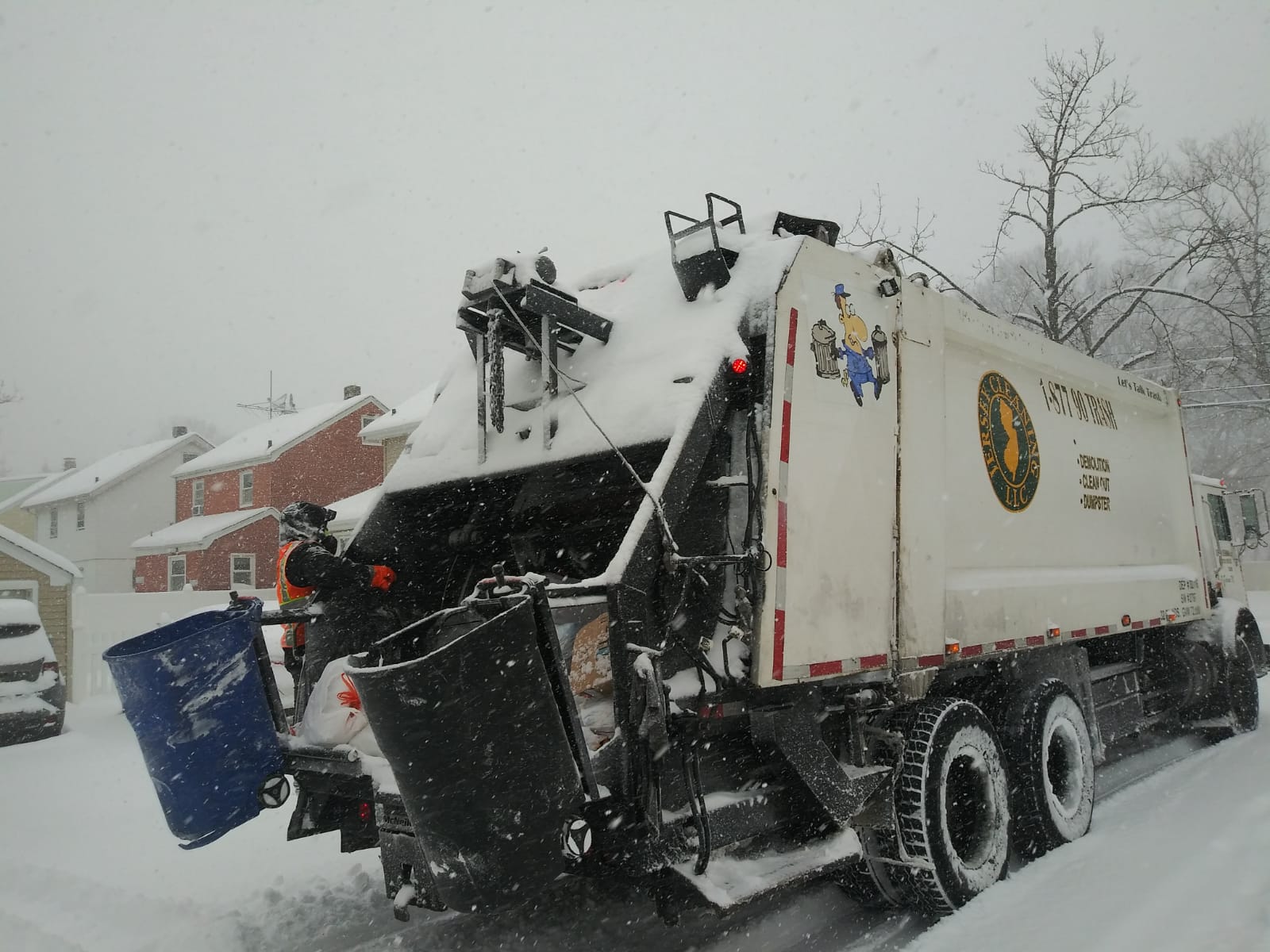 A garbage truck is parked in the snow with the lid open