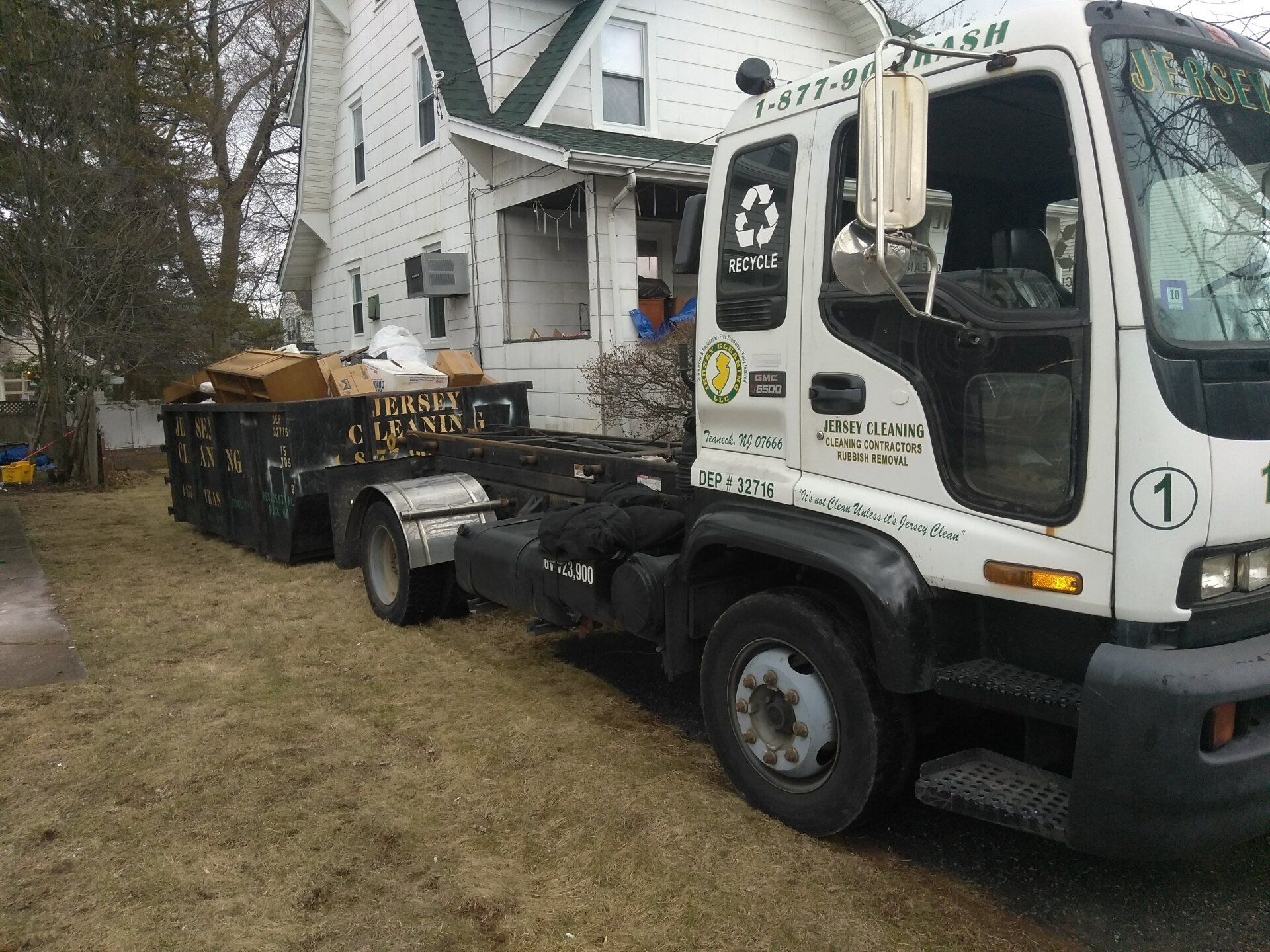 A dumpster filled with boxes and a sign that says Jersey Cleaning.