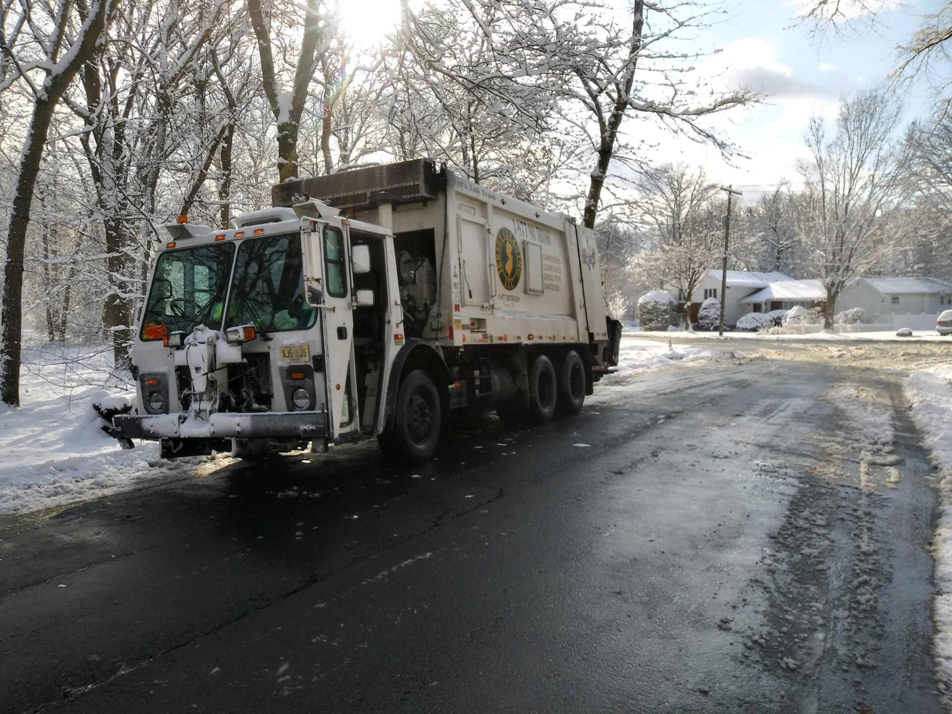 A garbage truck is driving down a snowy road.