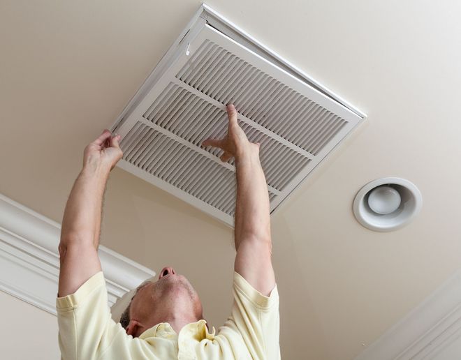 Person replacing a ceiling air filter beneath a vent in a white room