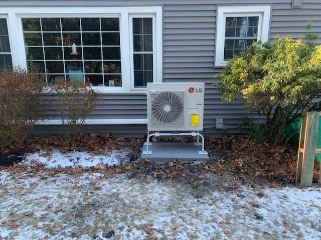 Outdoor LG HVAC unit beside a house window in a snowy yard