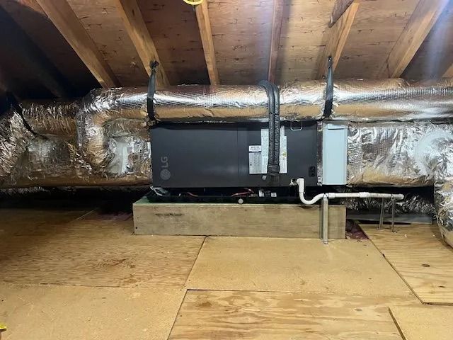 Black HVAC unit and insulated ductwork in an attic crawlspace under exposed wooden rafters.