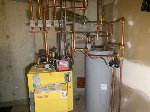 Basement with yellow boiler, gray water heater, and exposed copper piping against concrete walls