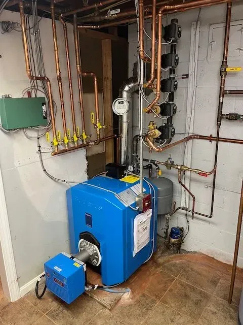 Blue boiler with copper pipes and control units in a utility room, shown against a wall with exposed plumbing.
