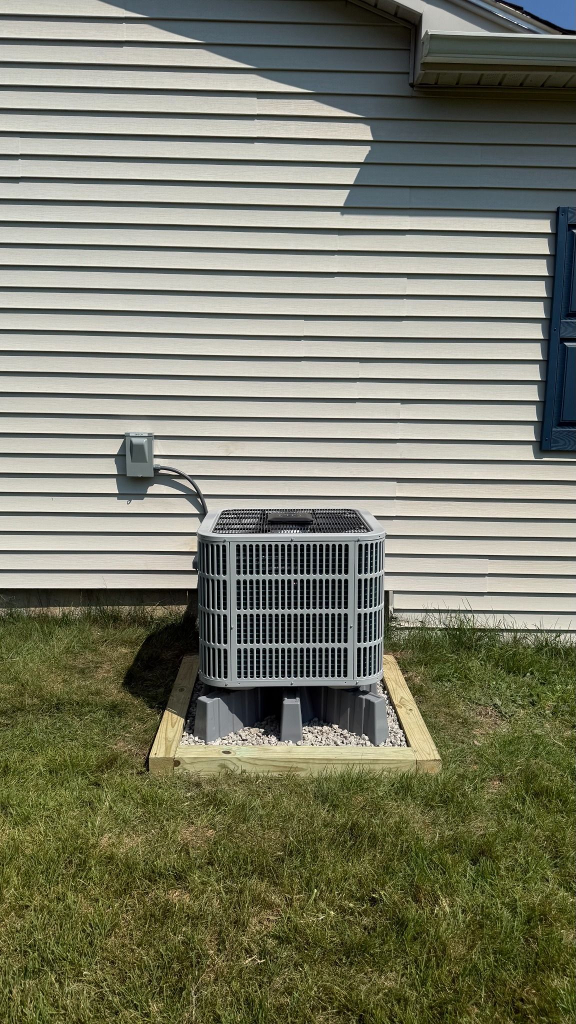 Outdoor air conditioner unit beside a beige house wall with vinyl siding and grass yard