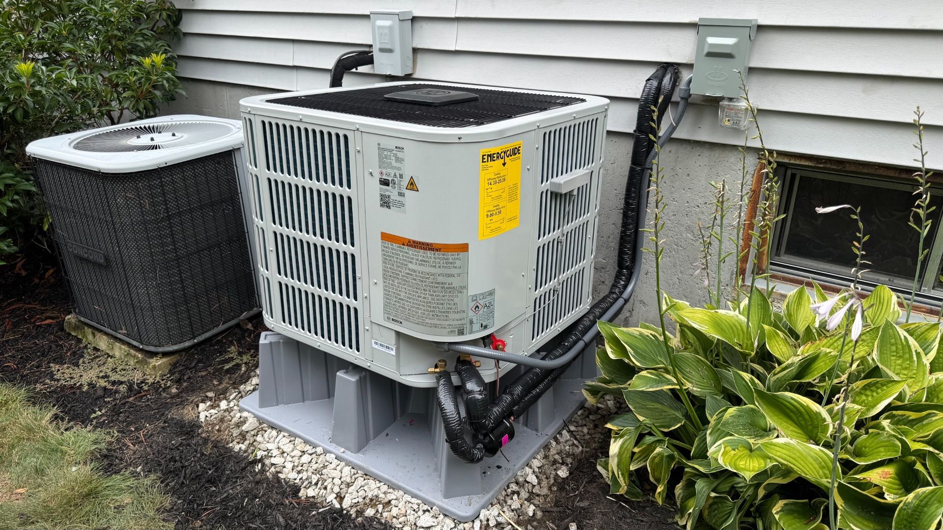 Outdoor HVAC unit beside a house, with ductwork and an air conditioner compressor on a concrete pad.