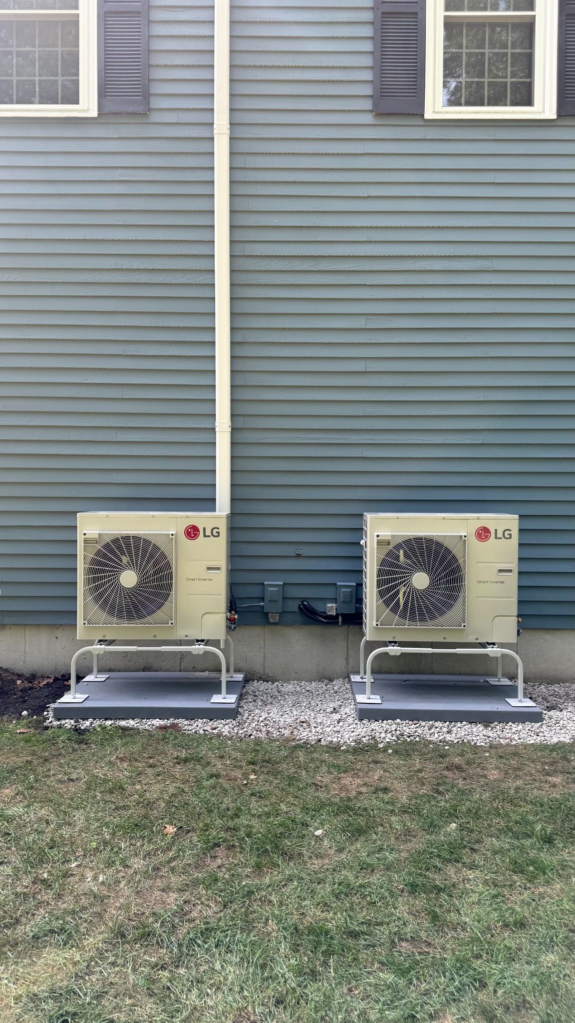 Two beige outdoor air conditioning units on concrete pads against a blue house exterior