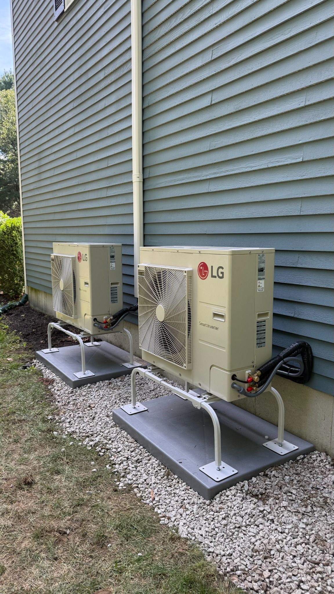 Two outdoor LG air conditioning units on concrete pads beside a house with gray siding.