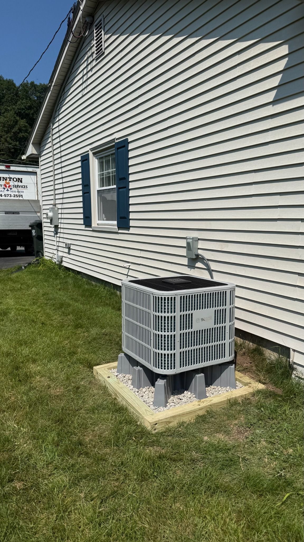 Outdoor air conditioner unit beside a beige house with white siding and green lawn