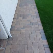 A brick walkway leading to a house next to a lush green lawn.