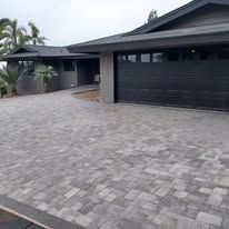 A house with a black garage door and a brick driveway in front of it.