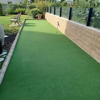 A putting green in a backyard with a wooden fence.