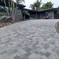 A brick driveway in front of a house with palm trees.