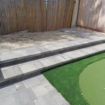 A patio with a putting green and a wooden fence in the background.