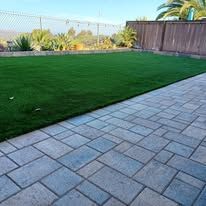 A patio with a lush green lawn and a fence in the background.