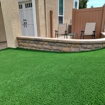 A lawn with a brick wall and chairs in front of a house.