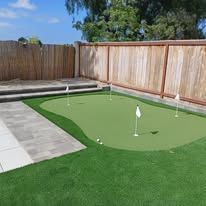 A backyard with a putting green and a wooden fence.