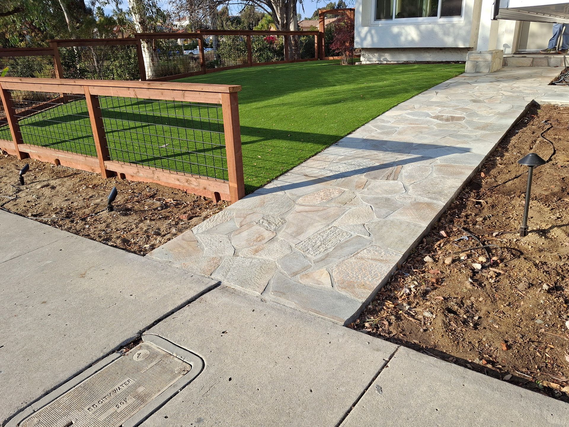 A stone walkway leading to a house with a wooden fence.