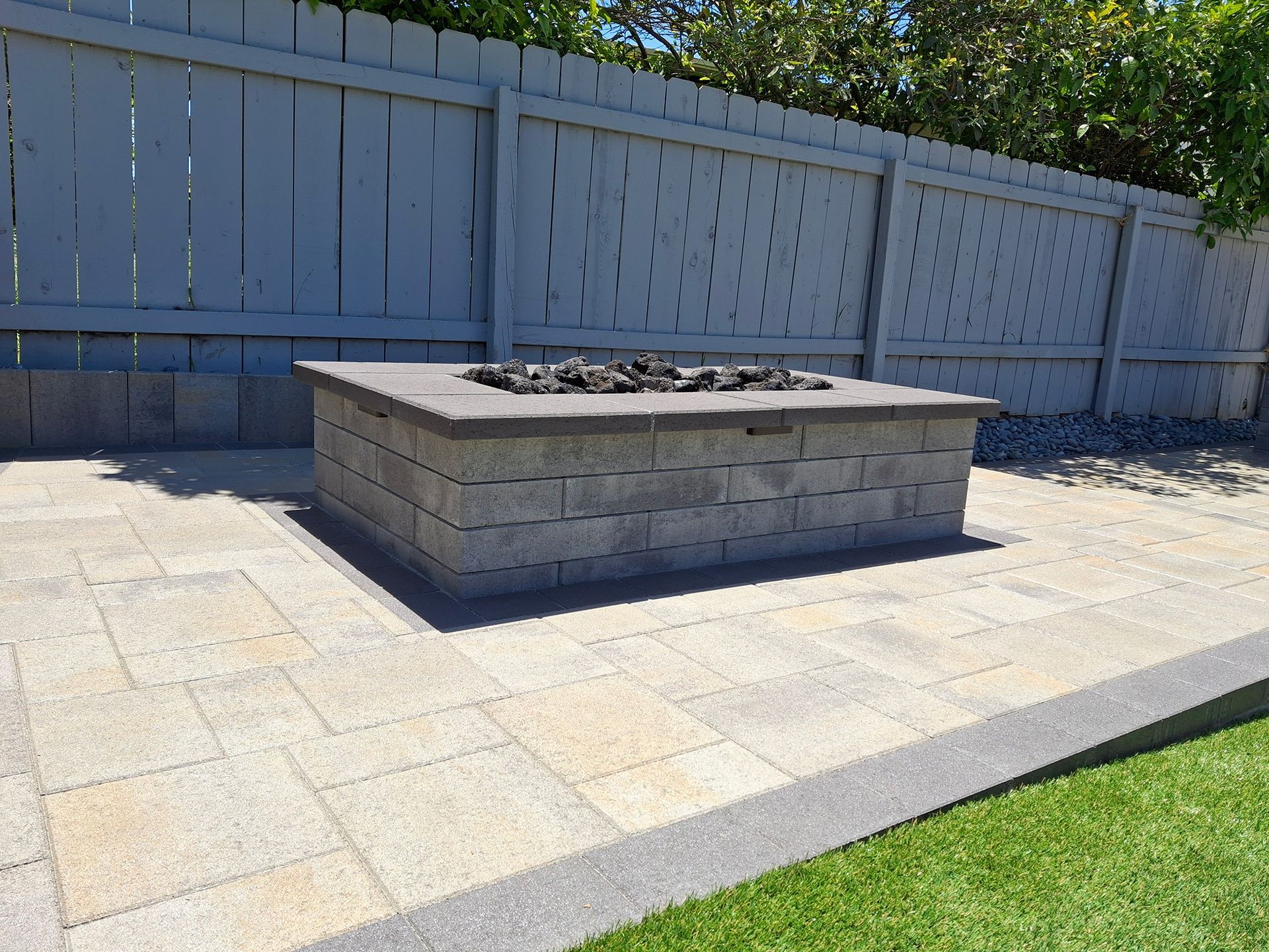 A fire pit is sitting on a patio next to a fence.