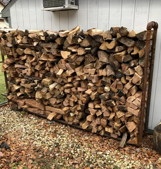 Stacked firewood piled against a house wall with a window air conditioner above it