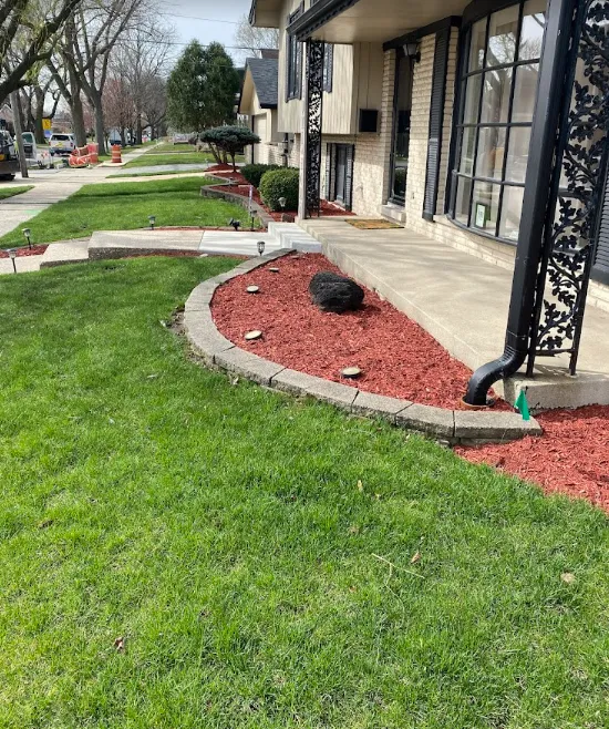 Apartment walkway with green lawn, red mulch beds, and building entrances along the sidewalk