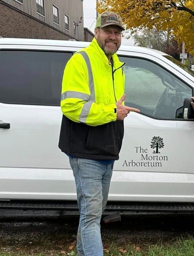 Man in neon yellow jacket stands beside a white van with The Morton Arboretum logo.