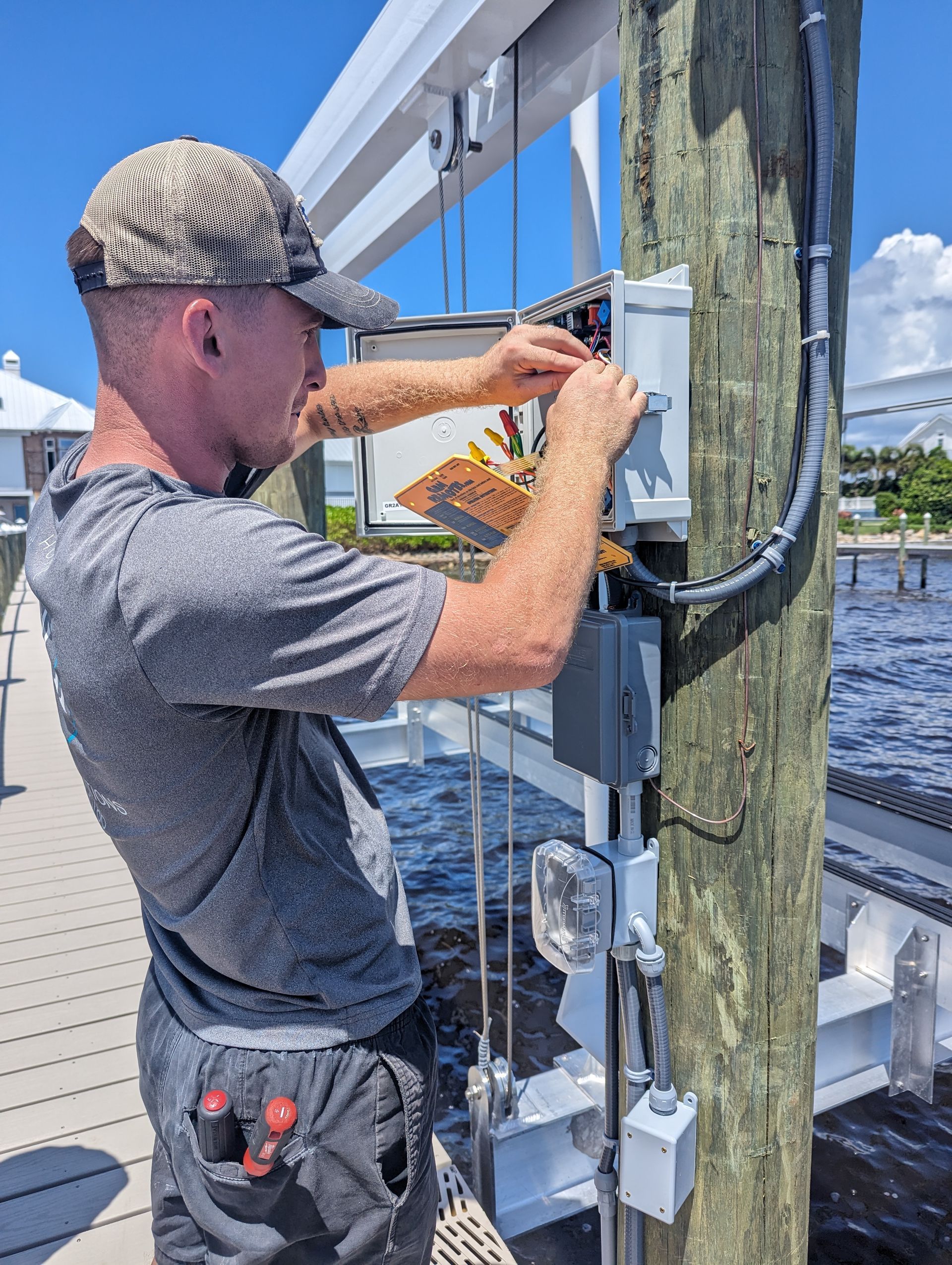 Man tightening a metal bracket on a dock post beside the water.