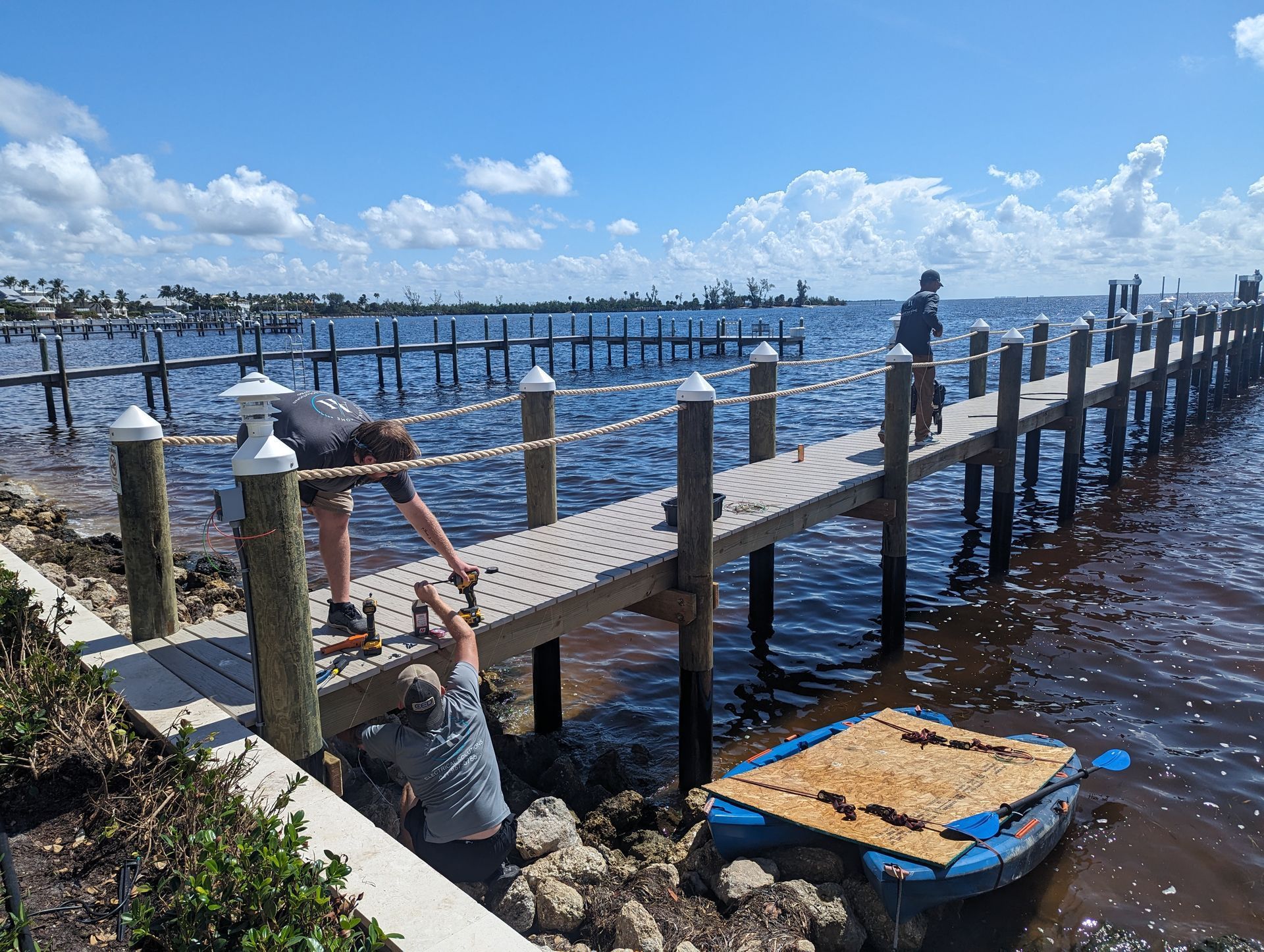 Wooden dock with railings extending over calm water under a bright blue sky, with a person at the left edge.