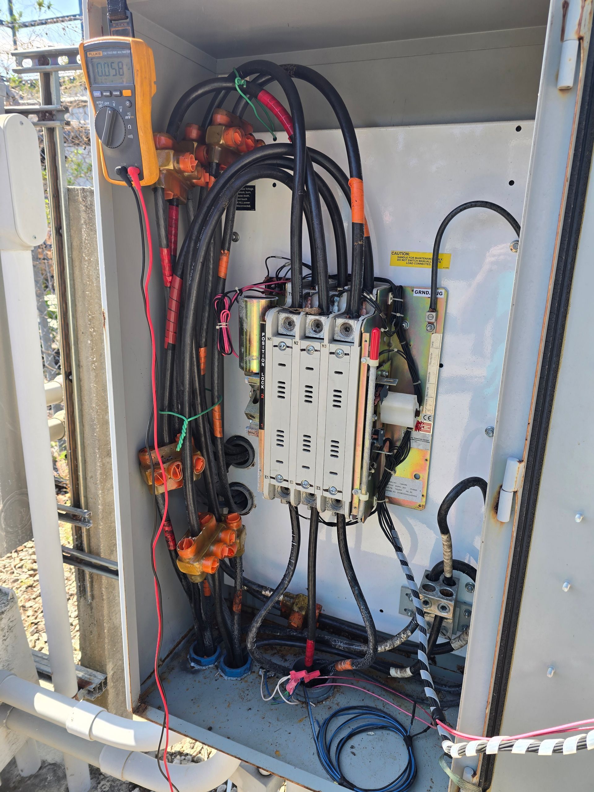 Open electrical control panel with wires, relays, and breakers mounted inside a metal cabinet.
