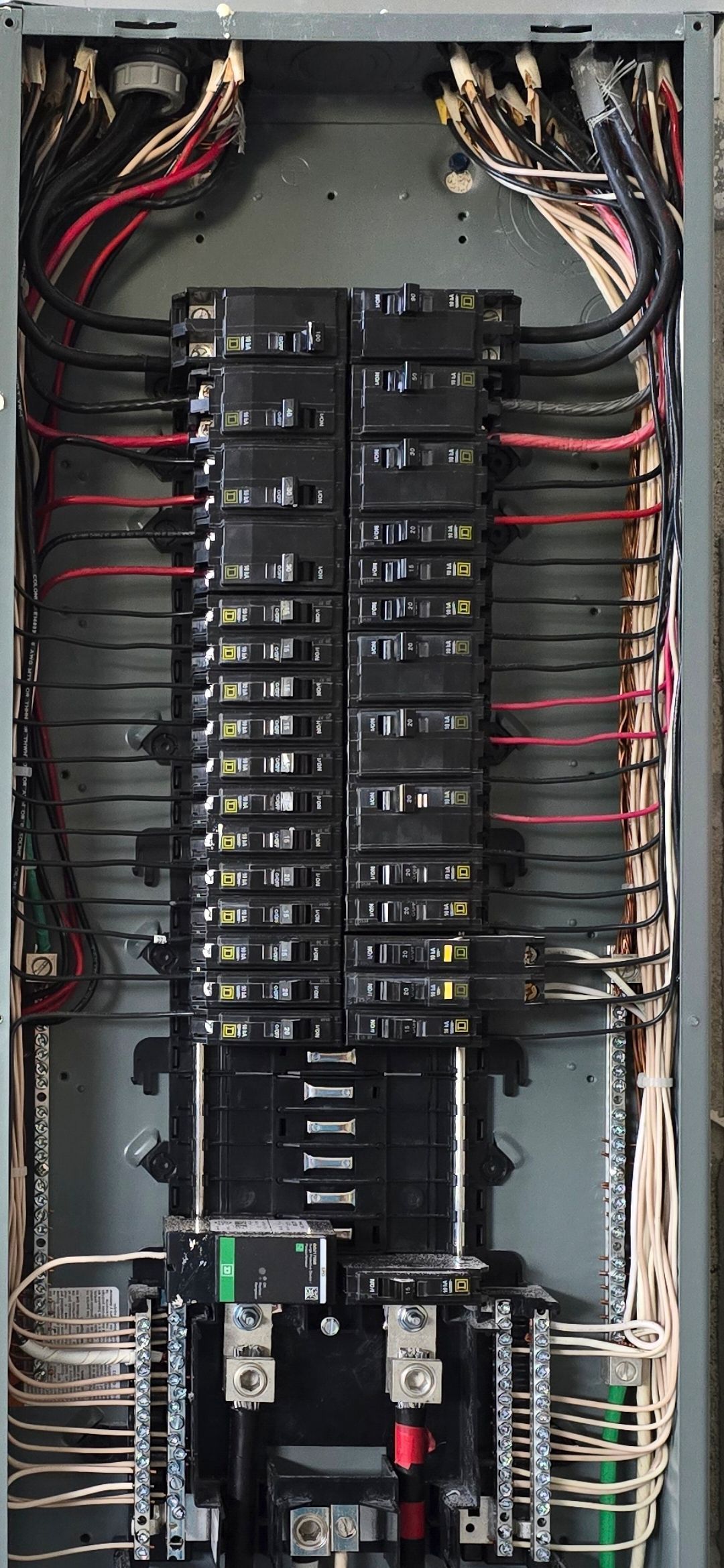 Open electrical breaker panel with rows of black breakers and red/white wiring inside a metal cabinet.