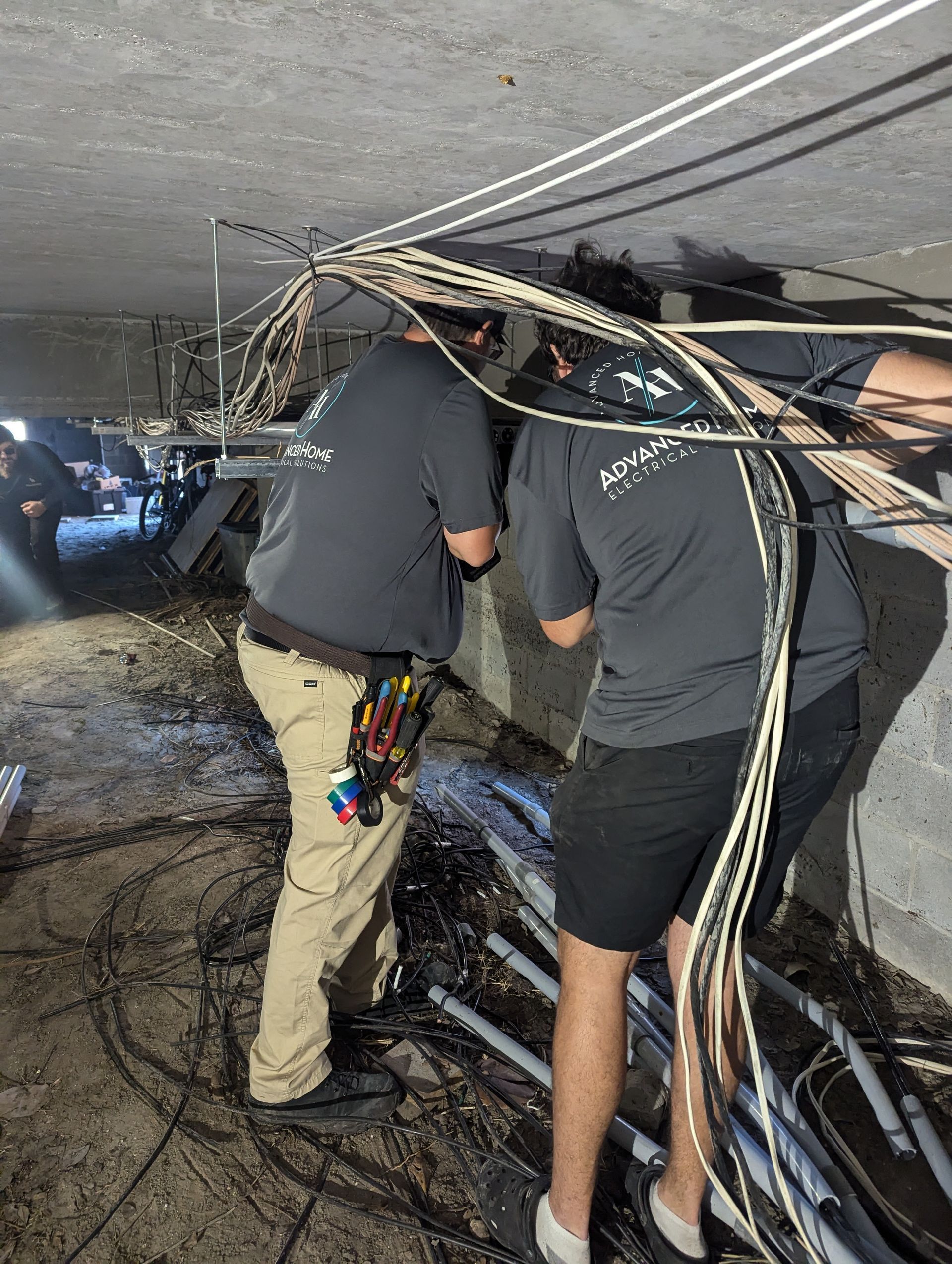 Workers inspecting tangled cables in a crawlspace beneath a building