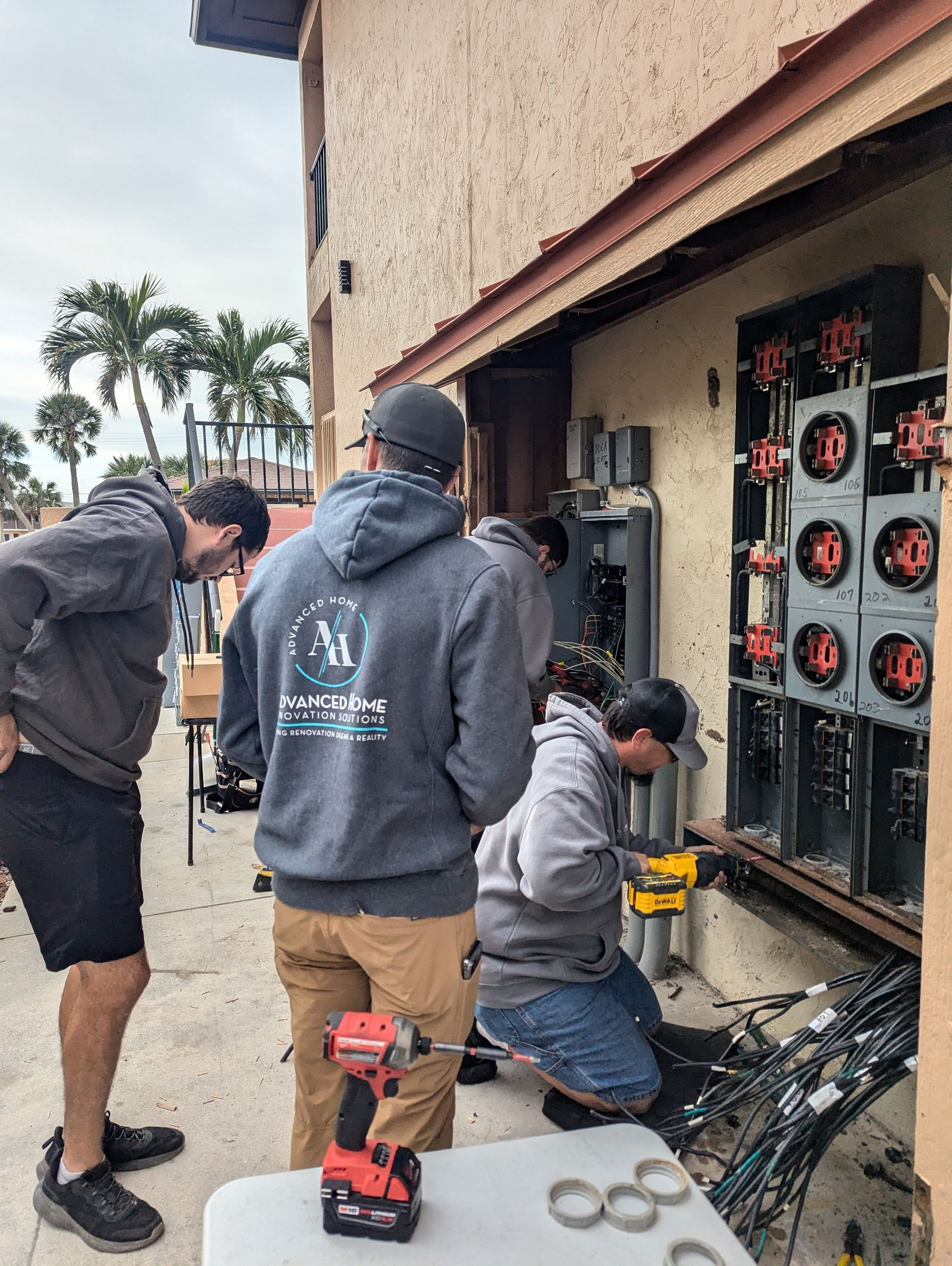 Three workers inspect and repair outdoor electrical panels beside a building