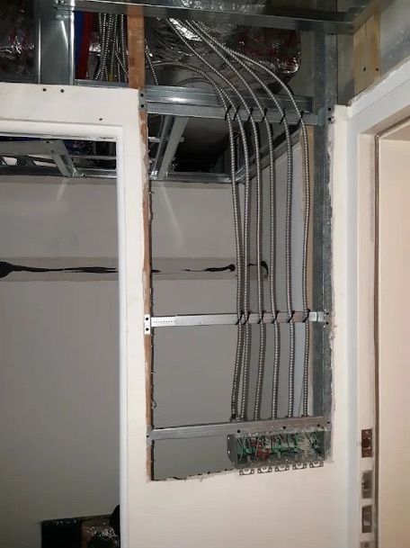 Open electrical panel with multiple gray conduits and wiring in a wall cavity