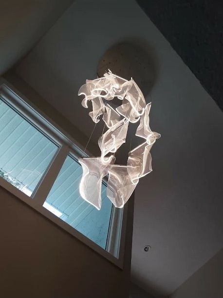 Abstract white hanging sculpture near a window, viewed from below on a ceiling.