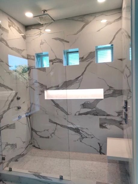 Marble-tiled shower with glass door, wall niche, three frosted windows, and overhead light