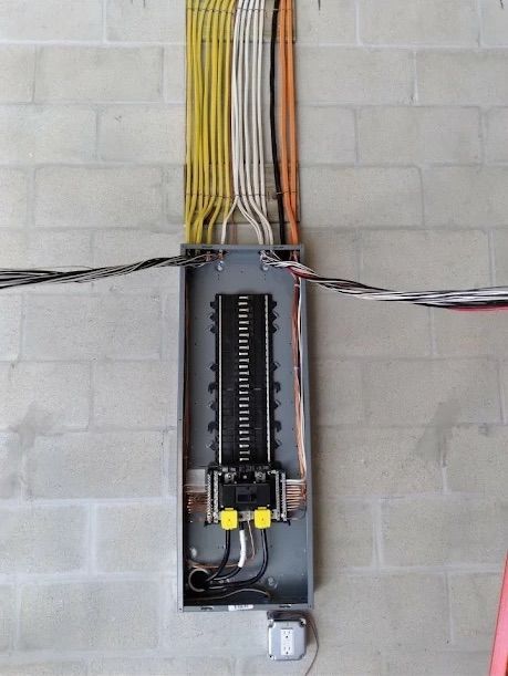 Open electrical breaker panel with colored wires on a cinder block wall