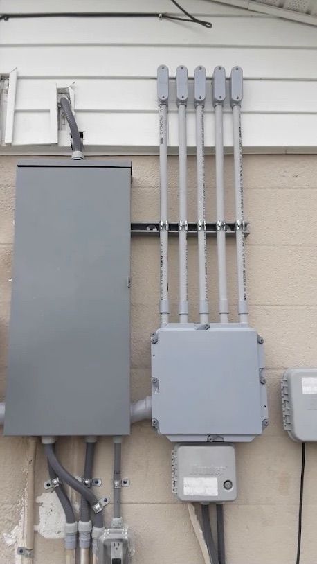 Gray utility boxes and electrical conduits mounted on an exterior building wall.