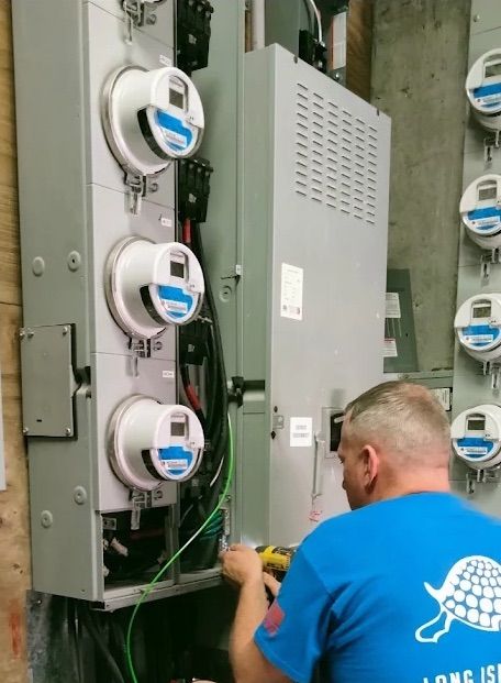 Technician in blue shirt works on electric meters in a utility panel room