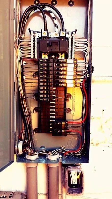 Open electrical breaker panel with wiring, switches, and conduits inside a metal box.