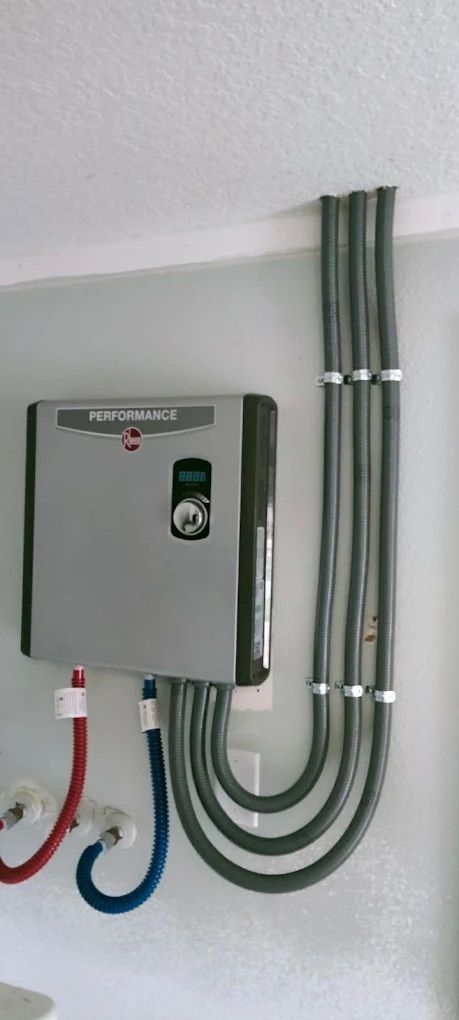 Gray electrical control box with green indicator, mounted on a wall with blue, red, and gray conduit pipes.